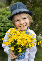 portrait of a cute joyful Ukrainian boy 6-7 years old in a traditional embroidered shirt, hat and with a bouquet of buttercups. Children for peace. stop the war. Pride to be Ukrainian. Mothers Day