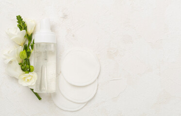 Cosmetic bottle with flowers on concrete background, top view