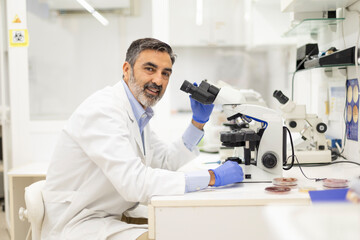 Smiling male scientist using microscope in a research laboratory