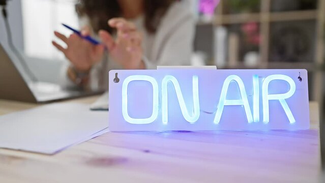 Illuminated 'on air' sign in a radio studio with a blurred woman gesturing during a broadcast.