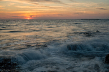 Tramonto sul mare, tra gli scoglie con l'acqua ad effetto seta.