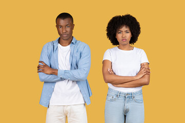 A young African American couple stands facing the camera with serious expressions and arms crossed