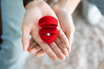 Boyfriend hand presenting a beautiful diamond engagement ring in a classic red velvet jewelry box...