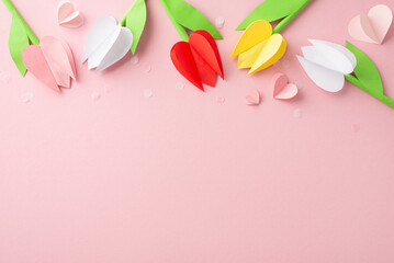 Celebrating moms with crafted affection. Top view of origami tulips, and heart shapes amid delicate confetti on a light pink surface, providing a blank area for text or advertising