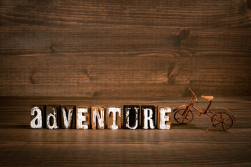 ADVENTURE. Text from alphabet blocks and rusty miniature bicycle on wood texture background