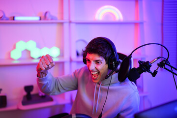 A joyful young man is engaged in online gaming culture while wearing headset with microphone and...