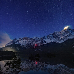 landscape of a snow-covered mountain range  at night with the starry sky above and the reflection over the lake at night in Bavaria