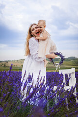 A happy mother hugs her daughter and smiles while standing near a white chair in a lavender field