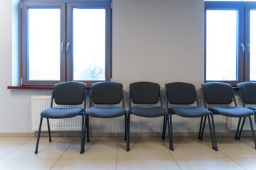 A row of black chairs in an empty waiting room. An empty room with chairs and large windows in the office.