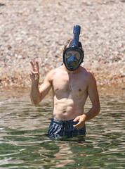 Muscular man standing in water up to their waist wearing dark swim trunks and a snorkeling mask...