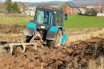 a blue tractor is plowing a field with a fence in the background.