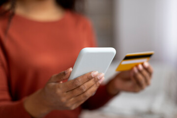 Closeup of young black woman's hands holding smartphone and credit card,