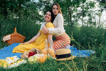 Pair of young ladies on a blue blanket, having a picnic in nature.