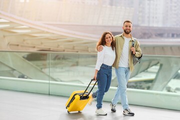 Fototapeta na wymiar Time For Trip. Happy European Couple Walking With Luggage At Airport Terminal