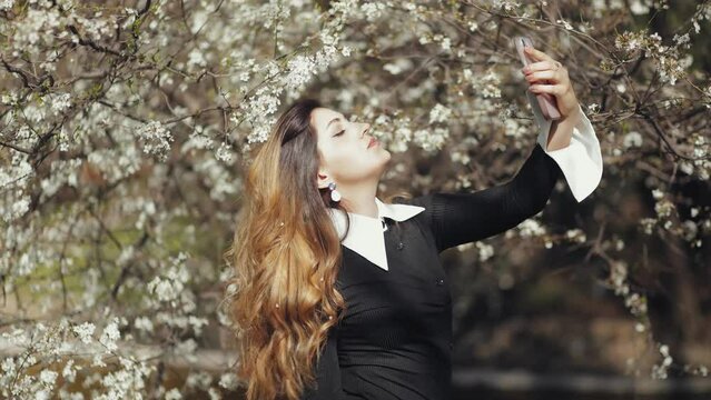 Beautiful girl takes a selfie at the cherry blossom festival, tree blossoms, flowers, spring beauty and freshness, new season and cycle, sakura, nature, sun, weather, meditation, relaxation