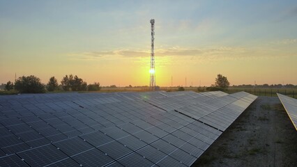 Photovoltaic solar panels at solar farm during golden hour with 5G telecom tower in the background © TechAnimationStock