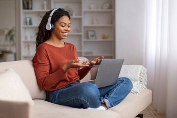 Young black woman wearing headphones gesturing during video call on her laptop