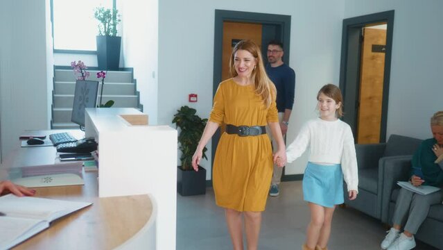 A family with a child leaves the pediatrician's office and approaches the reception, talking to a friendly nurse, leaving the medical clinic after a successful examination