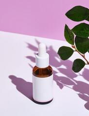 minimalist image showcasing a skincare essence bottle beside fresh green leaves on a dual-tone background. - 763108404