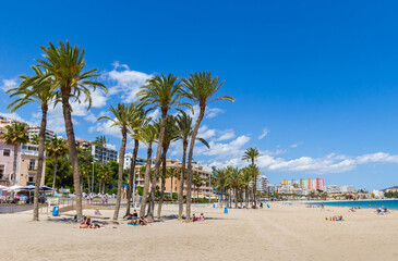 People relaxing under the palm trees on the beach in Villajoyosa, Spain - obrazy, fototapety, plakaty
