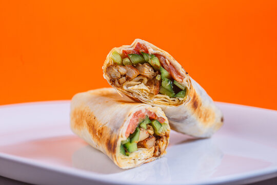 Chicken bacon ranch wrap cut in half on a white plate. Studio shot with orange background. Healthy eating and fast food alternative concept. Design for menu, poster, and banner.