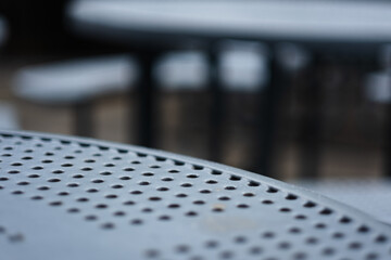 Closeup of the edge of a park table. The steel design has holes cut out to allow water to pass...