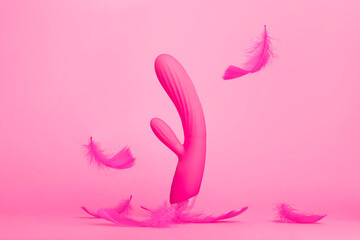 Pink sex toy rabbit shaped female vibrator for women isolated on pink background with feathers...