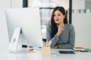 Fototapeta premium Portrait of professional millennial Asian businesswoman in casual attire analyzing financial data on her laptop computer in the office.