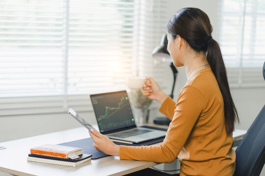 Relaxed stock exchange trader or businesswoman working with a stock market dashboard, analyzing trading data, graphs, and charts in a home office
