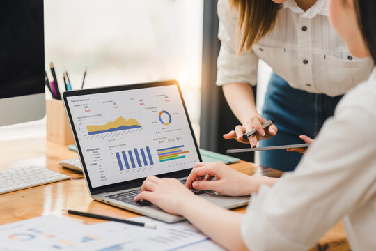 Two businesspeople or an accountant team are analyzing data charts, graphs, and a dashboard on a laptop screen in order to prepare a statistical report and discuss financial data in an office.
