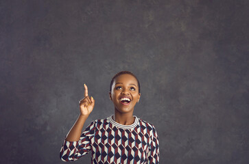 Happy emotional dark skinned woman who has great idea pointing her index finger up at copy space....