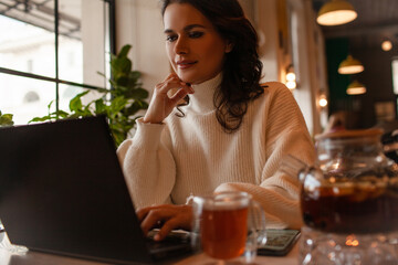 The girl works at the computer and drinks tea in cafe.