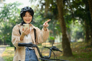 Smiling young woman riding an electric bicycle and using mobile phone for direction