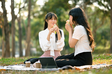 Shot of happy female co workers eating sandwiches on lunch break at outdoors