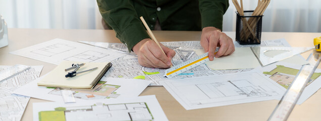 A portrait of architect using divider to measure blueprint. Architect designing house construction on a table at studio, with architectural equipment scattered around. Focus on hand. Delineation - obrazy, fototapety, plakaty