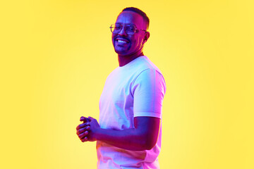 Portrait of smiling African-American man in glasses and white t-shirt standing against yellow...