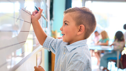 Male Primary Or Elementary School Student Writing On Whiteboard In Classroom Lesson