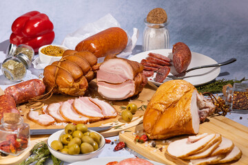 an abundance of meat delicacies on a concrete background surrounded by various spices and herbs, olives, peppers