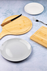 empty plates and serving and cutting boards on a light blue background, fork and knives nearby