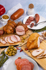 an abundance of meat delicacies on a concrete background surrounded by various spices and herbs, olives, peppers