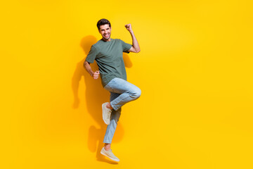 Fototapeta na wymiar Full length photo of positive lucky man dressed khaki t-shirt rising fists jumping high empty space isolated yellow color background