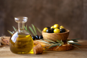 A bowl full of green and black olives, with an olive oil bottle, on a rustic wooden table. Bottle...