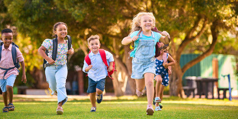 Multi-Cultural Primary Or Elementary School Students With Backpacks Running Outdoors At End Of Day