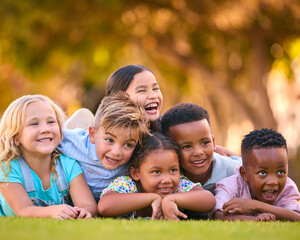 Portrait Of Multi-Cultural Primary Or Elementary School Student Friends Lying On Grass Outdoors - 763137402