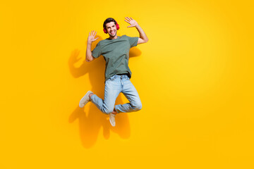 Full length photo of funky cool guy wear khaki t-shirt jumping high listen songs headphones empty...