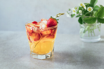 Refreshing orange summer drink with strawberry slices and ice cubes; fizz cocktail served in short glass with simple garnish on skewer front view close up