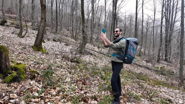 Solo male hiker takes a selfie and makes video call in a forest with his backpack.