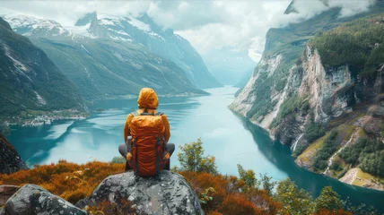 Fototapeten Traveler with backpack gazes at lake from rock in natural landscape © AlexanderD