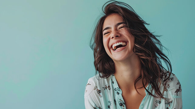 Young woman laughing at a good joke on pastel blue background
