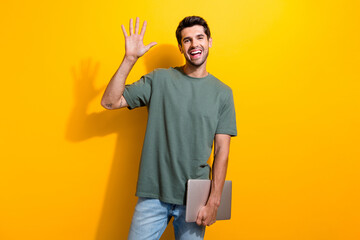 Portrait of pleasant nice guy with stubble wear stylish t-shirt hold laptop waving palm say hi...